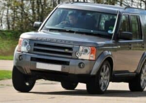 Xe ô tô bị nghiêng một bên khi đỗ và kỹ thuật viên VATS đang kiểm tra hệ thống treo gầm.