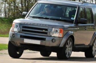 Xe ô tô bị nghiêng một bên khi đỗ và kỹ thuật viên VATS đang kiểm tra hệ thống treo gầm.